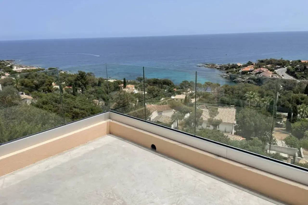 Vue panoramique sur une terrasse donnant sur la mer Méditerranée avec des maisons et des arbres en arrière-plan.