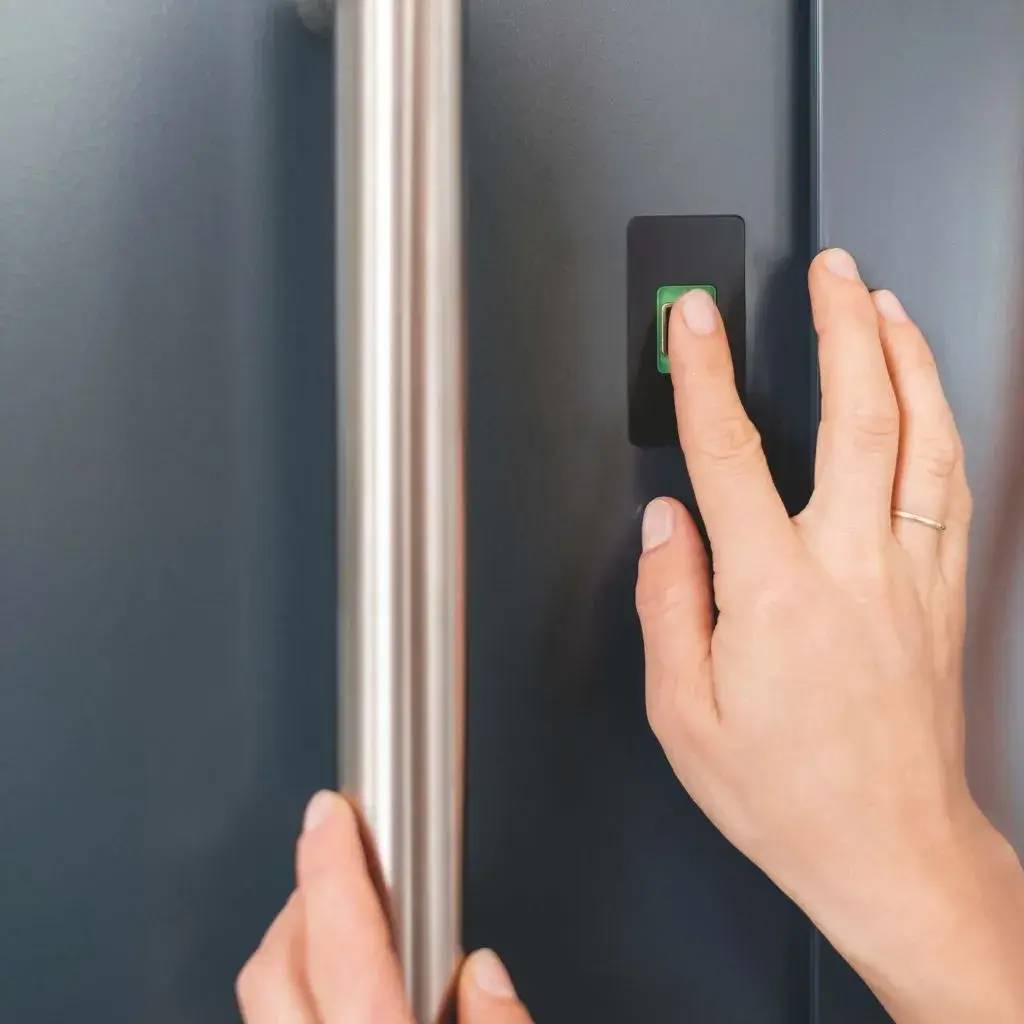Une main posée sur une poignée de porte métallique avec un doigt sur un capteur de reconnaissance d'empreinte digitale.