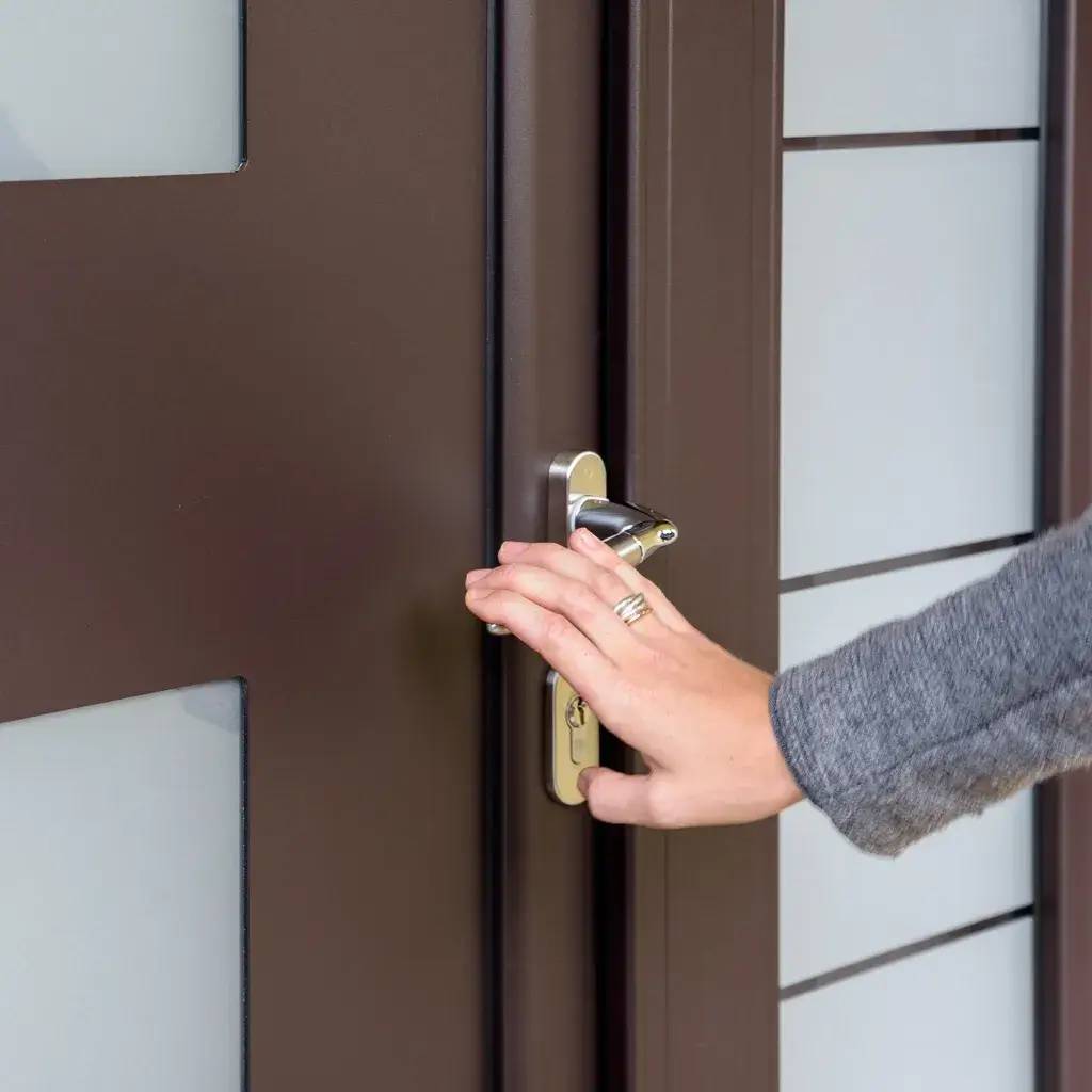 Une main s'apprête à ouvrir une porte en métal marron avec une serrure moderne.