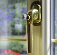 Poignée de fenêtre dorée avec vue sur un jardin fleuri à l'extérieur.